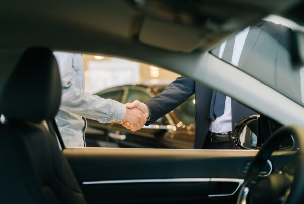 Buyer of car shaking hands with seller in auto dealership, view from interior of car. Close-up of handshake of business people. Concept of choosing and buying new car at showroom.